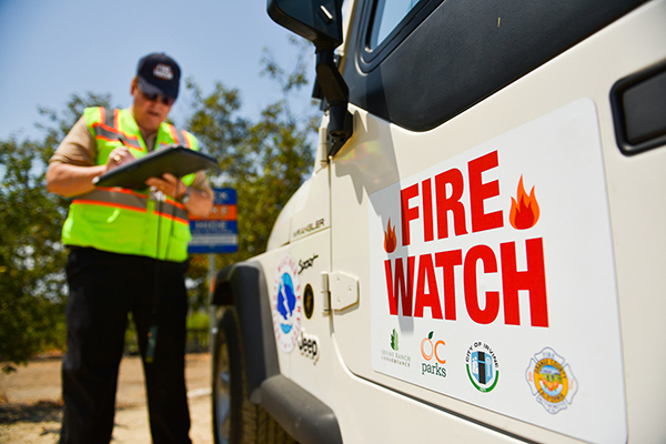 Man with safety vest writes on clipboard near a Fire Watch vehicle
